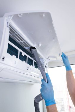 Havalandırma ünitesini vakum hortumuyla temizlerken mavi eldiven giyen birini gösteren detaylı bir görüntü, uygun bakım ve kapalı hava kalitesini sağlıyor..