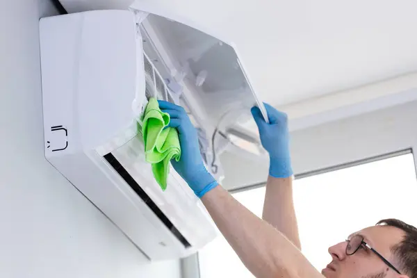 Klimayı kumaşla dikkatlice temizleyen bir birey, kapalı hava kalitesi ve sistem verimliliği açısından düzenli bakımın önemini vurgularken görülüyor..