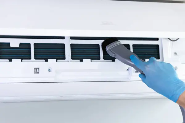 Mavi eldiven giyen bir kişi havalandırma ünitelerini temizliyor filtre ve bobinleri verimli soğutma ve hava filtrelemesini sağlamak için, kapalı ortamlarda daha iyi hava kalitesini teşvik ediyor.