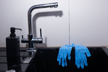 Bu resim, temiz ve işlevselliği vurgulayan, parlak bir el sabunluğunun yanına yerleştirilmiş, cilalı, mavi, tek kullanımlık eldivenli modern bir lavabo alanını gösteriyor..
