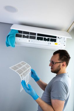 Mavi eldiven giyen bir adam birimini korurken klima filtresini yakından inceliyor. Uygun bakım, optimal performansı ve kapalı hava kalitesini güvence altına alır.