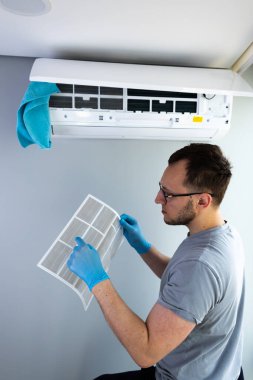 Bu resimde, çalışkan bir adam, modern yaşam alanları ve ev konforu optimal soğutma verimliliği için düzenli bakım önemini gösteren klima filtresini inceliyor..