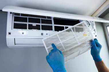 Bu görüntüde bir teknisyenin elleri mavi eldiven giyerken bir havalandırma ünitesinden filtre çıkardığı görülüyor. HVAC sistemlerinin düzgün bakımı verimlilik ve hava kalitesi açısından çok önemlidir..