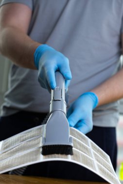 Görüntü, vakum eklentisiyle filtreyi temizleyen mavi eldivenli bir kişinin ev aletleri ve hava kalitesi için temel hijyen ve bakım uygulamasını vurguluyor..