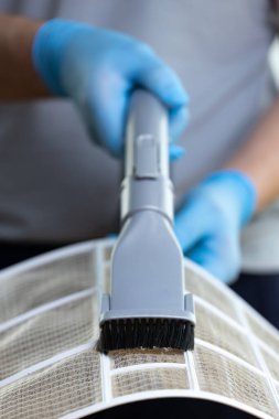 Mavi eldiven giyen biri, hava filtresini temizlemek için fırça eklentisi kullanıyor. Projede temizliğin sağlanması ve evdeki havalandırma sistemlerinin verimliliğinin korunması üzerinde duruluyor..