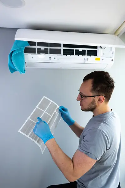 Bu resimde, çalışkan bir adam, modern yaşam alanları ve ev konforu optimal soğutma verimliliği için düzenli bakım önemini gösteren klima filtresini inceliyor..