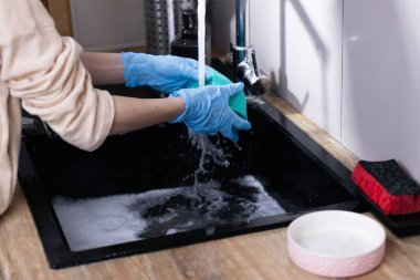 Eldivenli ellerin köpüklerle dolu bir lavaboda sünger yıkadığı mutfak işine bir göz atmak, günlük ev işlerinde temizlik ve hijyenin önemini vurgulamak..