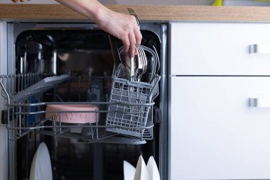 Bu resimde bulaşık makinesine çatal yerleştiren bir el, verimli ev temizliği rutinlerini ve modern aletlerin mutfaklardaki bulaşık yıkama görevlerini nasıl basitleştirdiğini gösteriyor..