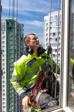 Yüksek görüş mesafesi olan bir pencere temizleyicisi, aşağıdaki hareketli şehrin üzerinde asılı dururken, yüksek bir binada çalışarak, kentsel yaşam ve güvenlik uygulamalarını ön plana çıkarıyor..