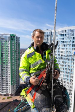 Cesur bir işçi güvenli bir şekilde dizginlenmiş, hareketli bir şehre tepeden bakıyor, modern mimari ve canlı çevrenin ortasında kararlılık ve direnç sergiliyor..