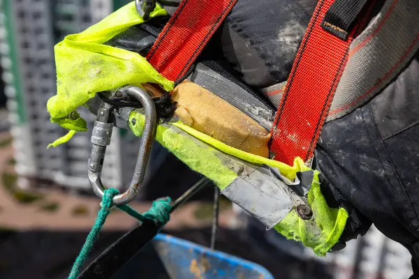 Yüksek irtifa görevlerinde korunmak için kullanılan parlak sarı bir kayış ve metal karabina ile yıpranmış bir emniyet kemerini gösteren ayrıntılı görünüm, işçi güvenliğini sembolize ediyor.