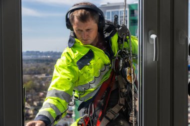 Becerikli bir pencere temizleyicisinin yüksek bir binada özenle çalıştığı, güvenlik donanımı giydiği, bakım ve temizlik araçlarıyla ipe asılı kalırken kaliteli hizmet verdiği görülüyor..