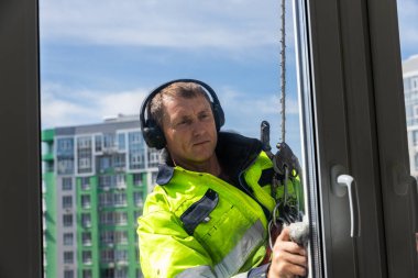 Bu resim, açık mavi gökyüzü altındaki çok katlı bir binanın pencerelerini özenle temizleyen güvenlik ekipmanlarıyla donatılmış yetenekli bir pencere temizleyicisini yakalar..
