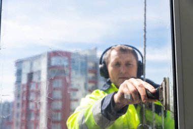 Görüntü, cam yüzeyini titizlikle silecek olan kendini adamış bir profesyonel pencere temizleyicisini gösteriyor. Açık hava manzarası sağlama üzerine yoğunlaşmasını vurguluyor..
