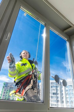 Kendini adamış bir cam temizleyicisi, temizlik için araç gereçleri kullanırken yüksek binaların dışında asılı kalan görevini yerine getirir. Parlak mavi gökyüzü eserleri için çarpıcı bir zemin sağlar..