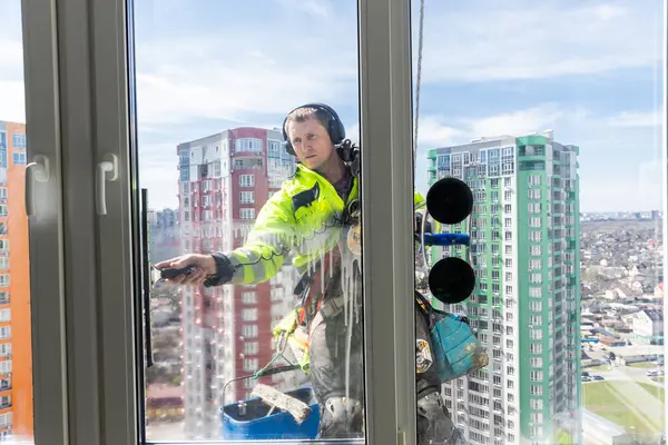 Yetenekli bir cam temizleyicisi yüksek irtifada cam temizlerken güvenlik donanımı takar ve kentsel ortamları güvenli ve güzel tutmada bakım işçilerinin hayati rolünü vurgular..
