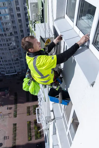 Yetenekli bir cam temizleyicisi titizlikle yüksek bir binanın yan tarafında çalışır. Camların parlak ve temiz olmasını sağlarken uygun güvenlik ekipmanları kullanır..