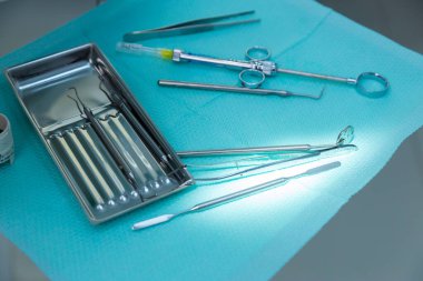 Bu resim, klinik bir ortamda diş işlemleri için gerekli araçları gösteren açık mavi bir yüzey üzerinde düzenli olarak düzenlenmiş çeşitli diş aletlerini içerir..