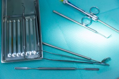 Bu resim, oral sağlıktaki önemlerini vurgulayan, bir turkuaz cerrahi yüzey üzerinde sistematik olarak düzenlenmiş ayna ve sondalar da dahil olmak üzere bir dizi diş aletini gösteriyor..