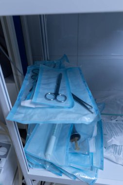 Görüntü çeşitli sterilize cerrahi aletleri sergiliyor mavi ambalaja sarılmış, tıbbi depolama alanında dikkatlice düzenlenmiş, sağlık ortamlarında hijyenin önemini vurgulayan.
