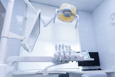 Bu resim, gelişmiş diş donanımı, parlak bir lamba, dijital monitörler ve optimal hasta bakımı için temiz ve düzenli bir ortam gösteren modern bir diş kliniği kurulumunu göstermektedir..