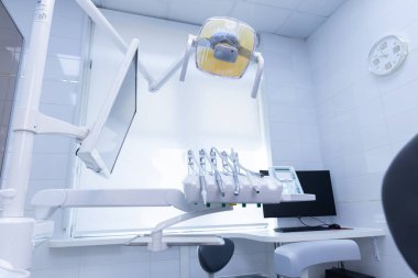 Görüntü, dişçi koltuğu, monitör, diş aletleri ve çevre aydınlatmasının yer aldığı çağdaş bir diş sağlığı kliniği gösteriyor, temiz ve rahat bir tedavi ortamını vurguluyor.