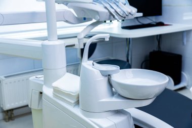 Görüntü, modern beyaz muayene koltuğu, durulama kabı ve hasta tedavisi ve bakımı için hazır yüksek teknolojili diş aletleri bulunan iyi donanımlı bir diş kliniğine sahip..