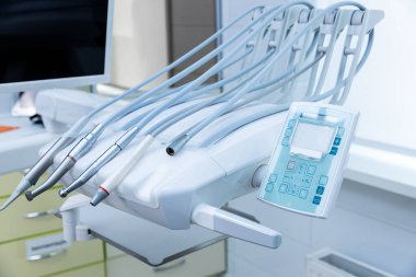 Bir tedavi istasyonundaki gelişmiş diş aletlerinin yakın plan görüntüsü, çeşitli el yazıları ve modern diş muayeneleri ve hasta bakımı için tasarlanmış dijital kontrol paneli sergileniyor.