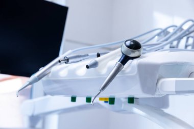 Bir diş kliniğindeki tedavi sandalyesine yerleştirilmiş gelişmiş diş aletlerinin yakından görüntüsü. Ortam, ağız sağlığı prosedürlerinde kullanılan teknolojiyi vurgulayarak iyi ışıklandırılmış..