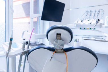 Görüntü, çağdaş bir dişçi koltuğu, çeşitli diş aletleri ve geniş bir monitörden oluşan, temiz ve hasta dostu bir alanı ön plana çıkaran parlak bir diş muayenehanesi gösteriyor..