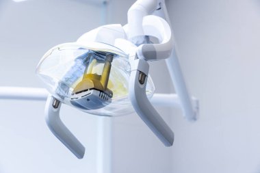 Görüntü gösterişli, çağdaş bir diş lambası armatürü sergiliyor. Şeffaf bir kılıf, ayarlanabilir kollar içerir ve modern bir klinikte dişçiye en uygun ışığı sağlamak için tasarlanmıştır..