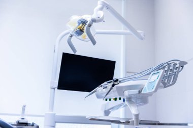 Çağdaş bir diş kliniğinde, diş hekimi koltuğu, ışık ve monitör, hasta rahatlığı ve bakımı için tasarlanmış temiz ve parlak bir ortamda gelişmiş teknolojiler sergiliyor..