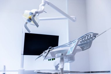 Görüntü, dişçi sandalyesiyle donatılmış çağdaş bir diş muayenehanesi, gelişmiş ışıklandırma ve diş tedavisine uygun davetkar bir atmosferi yansıtan bir monitör gösteriyor..