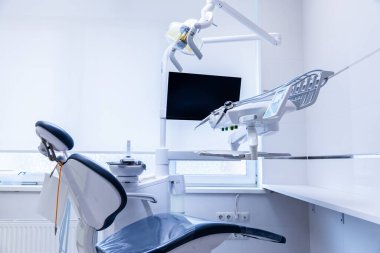Bu görüntü modern bir diş sağlığı kliniği yakalıyor. Son model bir dişçi koltuğu, tepe lambası ve monitör. Hepsi de hasta rahatlığını arttırmak için temiz ve iyi aydınlatılmış bir ortamda..