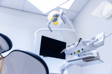 Görüntü, profesyonel bir klinik ortamında ileri diş ekipmanlarını sergiliyor, yukarıdaki ışık, monitör ve diş hekimliği gibi temel araçları vurguluyor ve hastanın rahatlığını sağlıyor..