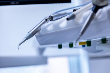 Klinik çalışma istasyonunda dişçilikte teknolojinin önemini yansıtan ve kullanılmaya hazır bir alet de dahil olmak üzere çeşitli gelişmiş diş aletlerinin yer aldığı bir resim..