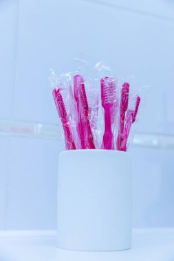 Bu resim, diş sağlığı ve ağız sağlığına karşı hijyenik ve şık bir yaklaşımı vurgulayarak beyaz bir kaba yerleştirilmiş çeşitli canlı pembe diş fırçalarını gösteriyor..