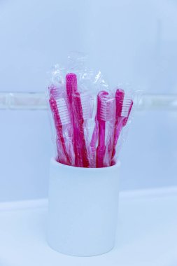 Bu resim, koruyucu plastiğe sarılı pembe diş fırçalarından oluşan bir çeşitlilik sergiliyor. Zarif bir şekilde, diş hijyen ayarları için ideal, parlak beyaz bir kapta sunuluyor..