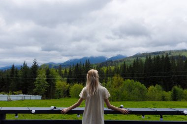 Genç bir kadının, bulutlarla kaplı dağların ve balkonundan yemyeşil ormanların çarpıcı manzarasının keyfini çıkararak huzurlu bir atmosfer oluşturduğu bir huzur anı..
