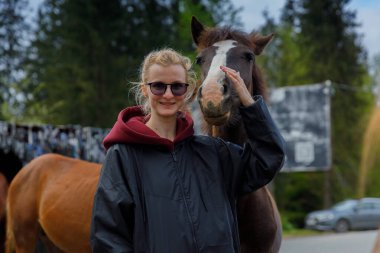 Görüntü, bir atla sevgiyle etkileşime girerken gülümseyen neşeli bir genç kadını yakalıyor. Barışçıl ortam, insanlar ve hayvanlar arasındaki bağın bir göstergesi..