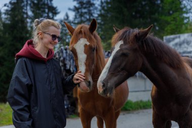 Görüntü, neşeli genç bir kadının iki atla neşe içinde etkileşime geçmesini ve sakin doğal ortamda insanlarla yaratıklar arasında güzel bir bağ olduğunu gösteriyor..