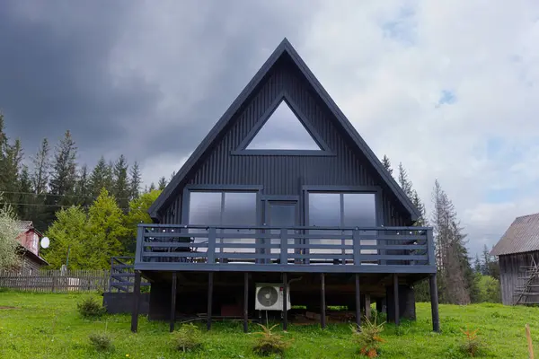 Bu çarpıcı A çerçeveli ev, modern tasarım ve doğal güzelliği uyumlu bir şekilde sergileyen büyüleyici bir orman zeminine karşı büyük pencereler ve şık siyah bir dış görünüme sahip..