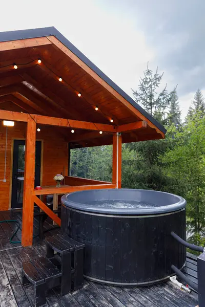 Bu resim, bereketli yeşillik ve rahat bir kulübe ile çevrili ahşap bir güvertede, dinlenmek ve doğanın güzelliğinden zevk almak için ideal, huzurlu bir jakuziyi gösteriyor..