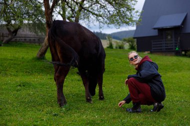 Güzel bir günde, bir kadın yemyeşil bir çiftlikte bir ineğin yanında çömelir, güneş gözlüğü takar ve doğanın güzelliği ve sükunetiyle dolu huzurlu ortamın tadını çıkarır..