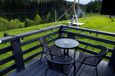 Bu resim zarif mobilyalarla süslenmiş büyüleyici bir balkon sergiliyor, güzel yemyeşil manzaranın ve hafif esintinin tadını çıkarırken rahatlatıcı bir doğa deneyimi sağlıyor..