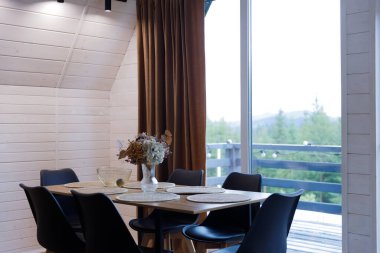 Modern bir masa seti ve zevkli bir dekorun sergilendiği davetkar bir yemek salonu. Geniş pencere, uzayın atmosferini ve sıcaklığını artırarak yemyeşil havanın çarpıcı bir görüntüsünü sunuyor..