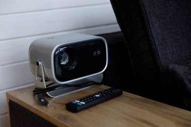 Çağdaş bir projektör, uzaktan kumandanın yanındaki ahşap bir masaya yerleştirilir ve sinemadan ve sunumlardan keyif almak için mükemmel bir atmosfer yaratır..
