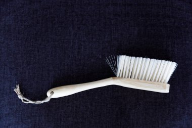 Bu resim sentetik kıllı minimalist ahşap bir fırça içeriyor, yüzeylerde etkili temizlik için tasarlanmış, kontrastlık ve görsel cazibe için koyu renk bir kumaş zemin üzerine yerleştirilmiş..