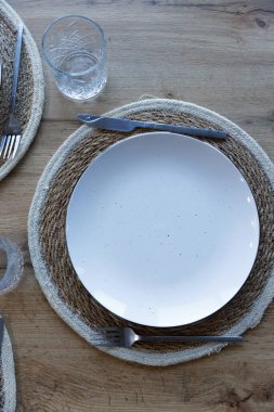 Bu resim, gümüş bir bıçak, çatal ve kristal bir bardakla tamamlanmış, dokuma bir plasemat üzerinde duran rafine bir masa üstü düzenini sergiliyor..