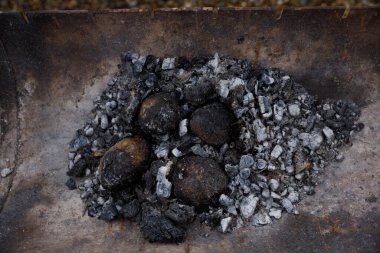 Görüntü, koyu kabuklar ve küller de dahil olmak üzere yanmış eşyaların kalıntılarını içeren metal bir kürek gösteriyor. Renklerin kontrastı sıcaklık ve ateşin sonrasını vurguluyor. Bu da yemek pişirme sahnesi olduğunu gösteriyor..